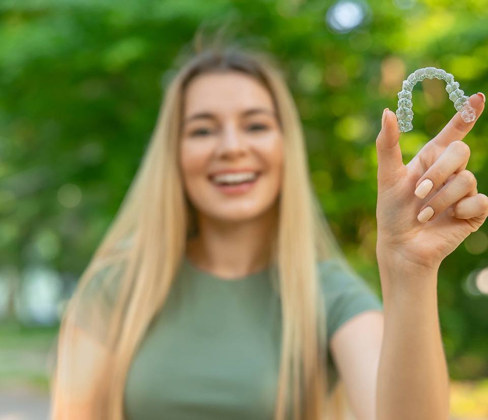 Teenage girl smiling while holding clear aligner