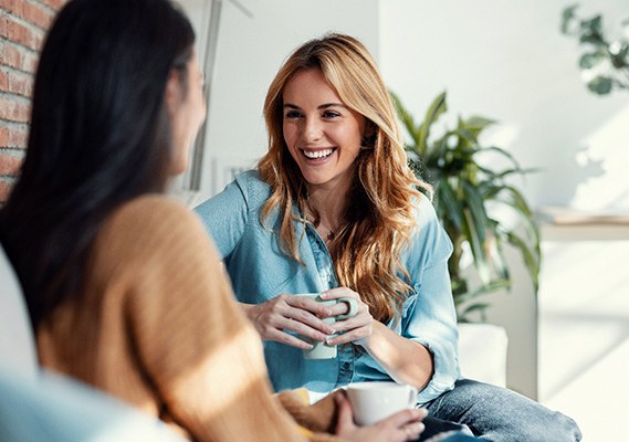 Woman smiling while drinking coffee with friend